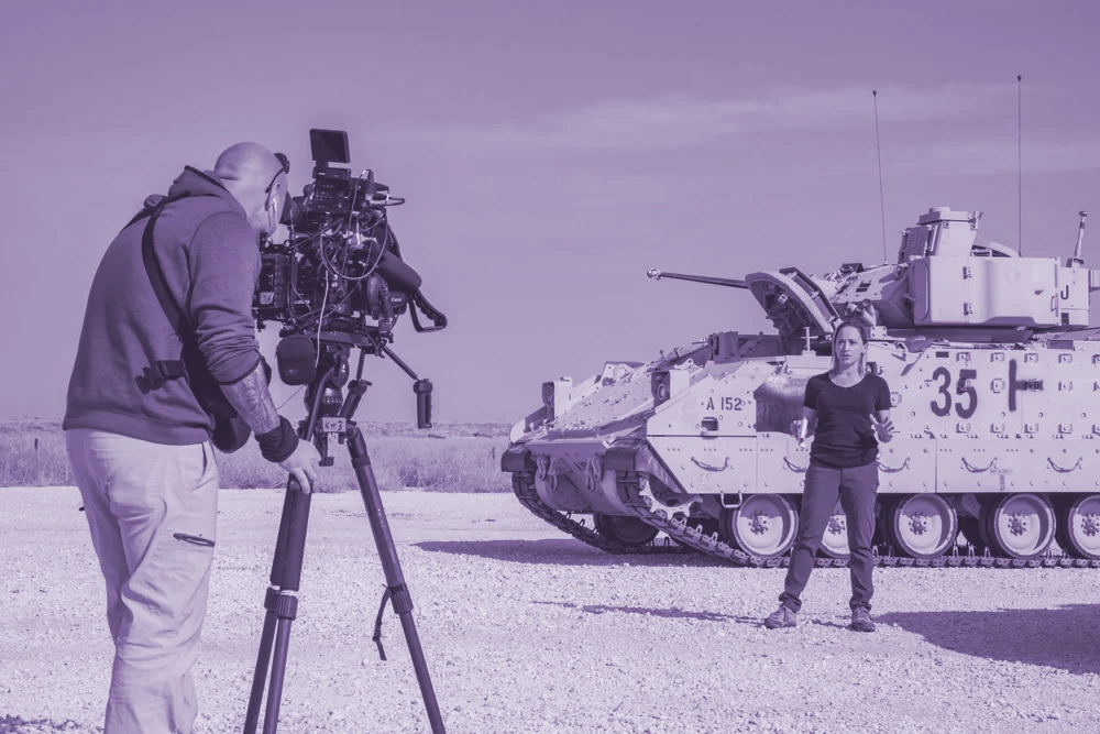 Military Reporters and Editors journalist in Syria reporting in front of tank and being filmed by photojournalist.